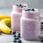 Tall glass of blueberry banana smoothie with blueberry and banana garnish.