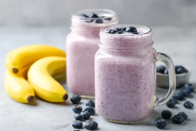 Tall glass of blueberry banana smoothie with blueberry and banana garnish.