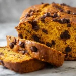Pumpkin chocolate chip bread loaf with slices and melty chips on a board