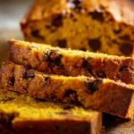 Pumpkin Chocolate Chip Bread loaf with slices and melty chips on a cooling rack