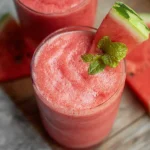 Refreshing watermelon smoothie in a glass with fresh fruit slices.