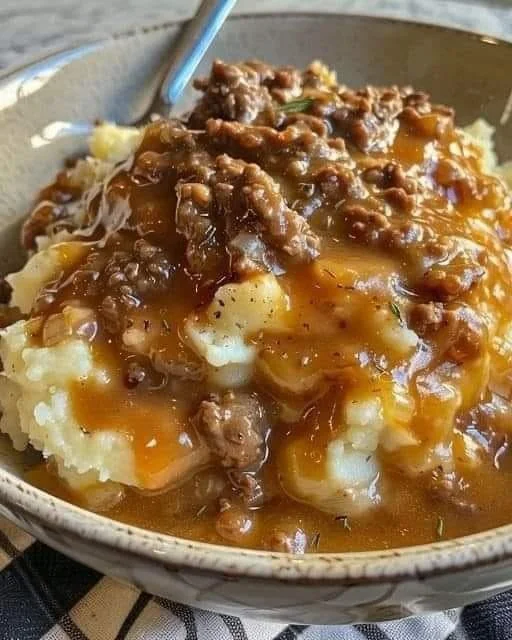Ground beef and gravy served over fluffy mashed potatoes in a bowl.